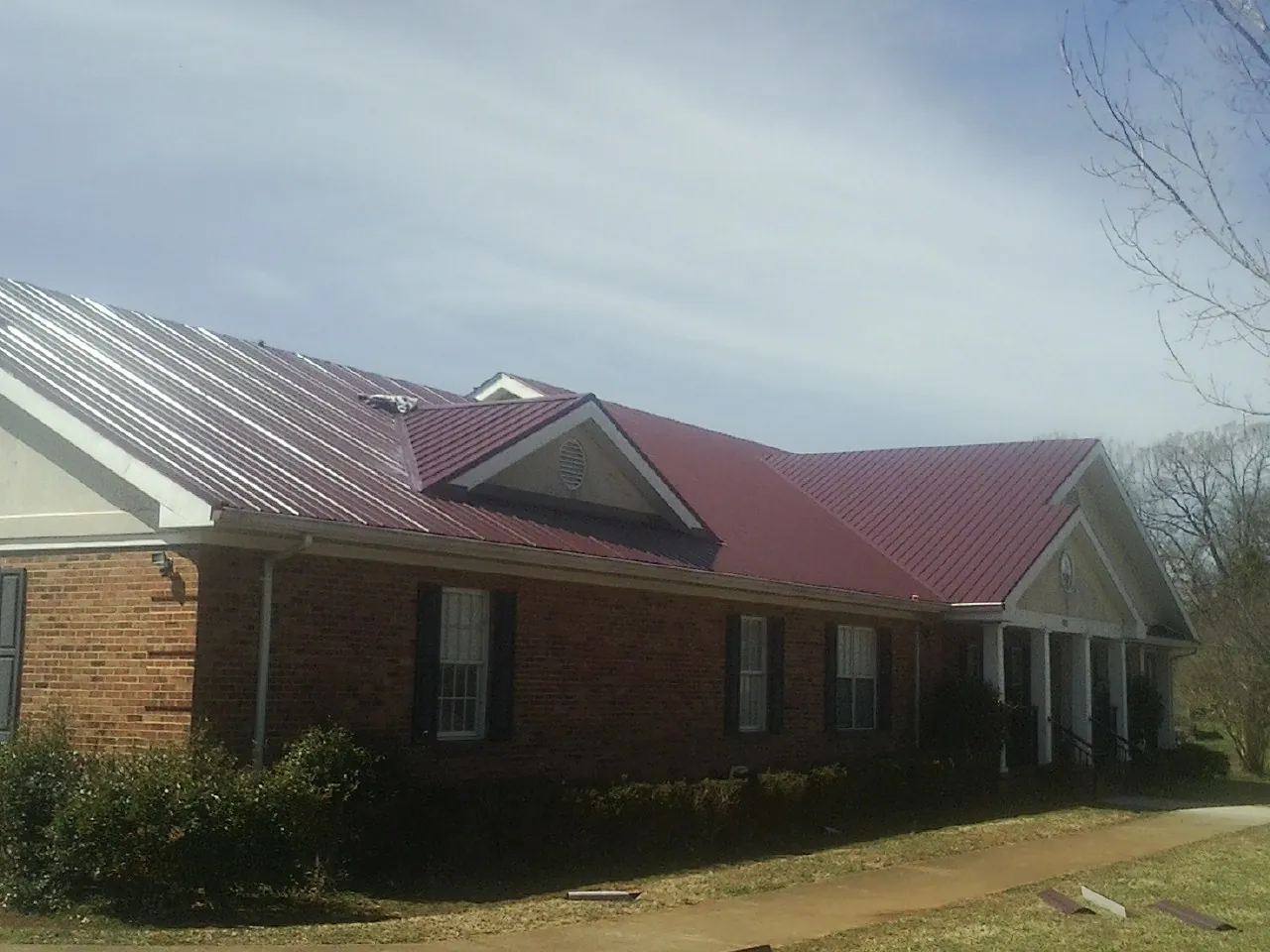 Red metal roof with gabled entries on a long brick building, from a Hail Damage Roof Repair job in Westhampton
