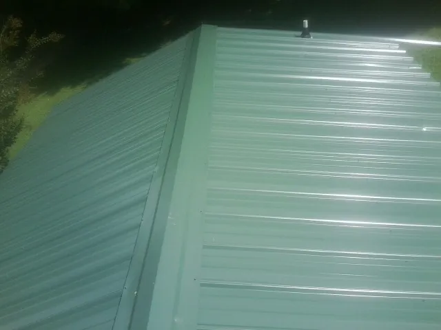 New green metal panels meeting at the ridge of a roof — Flat Roof Repair work by our crew in Westhampton
