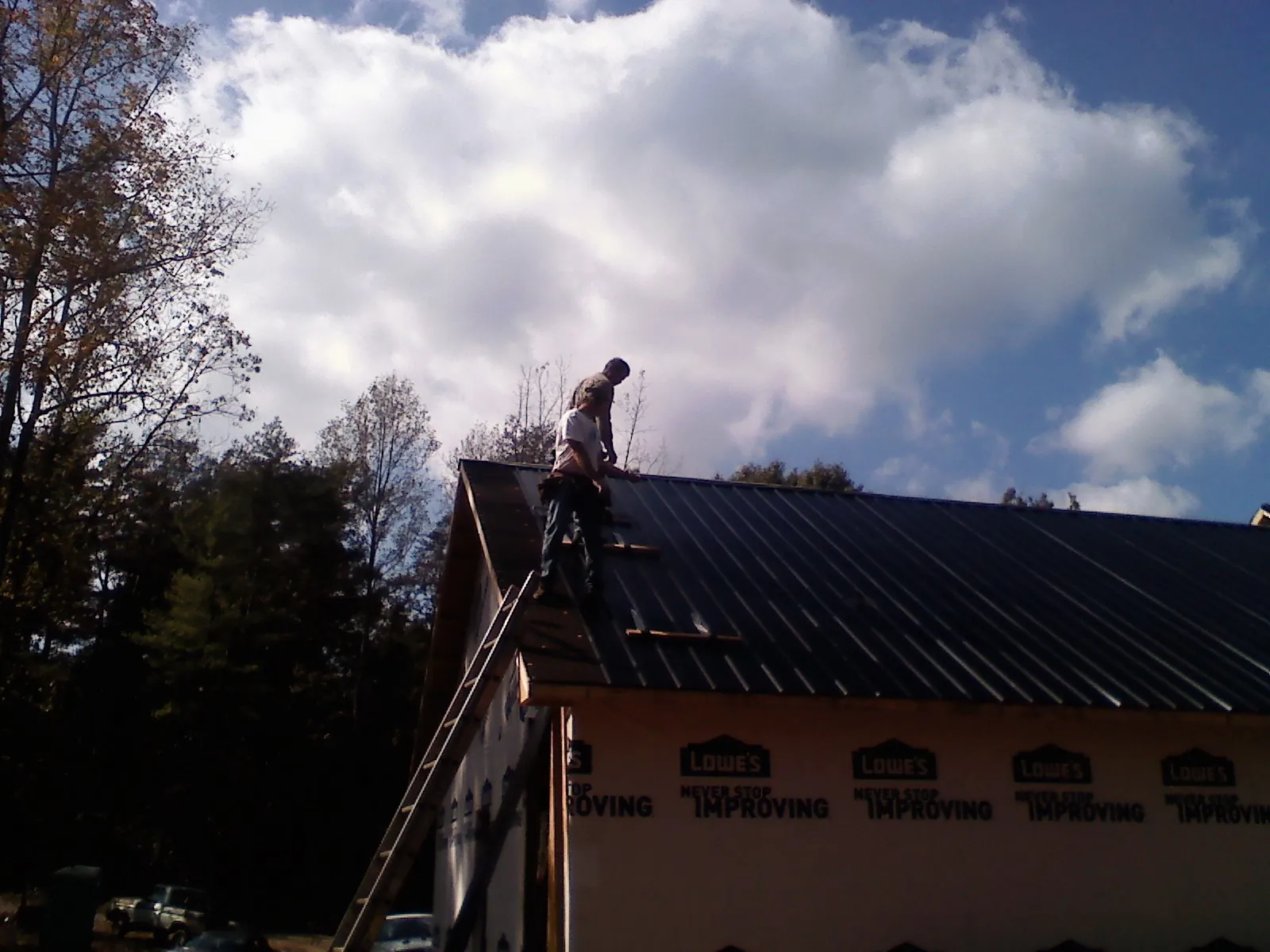 Roofer fastening dark metal panels high against a cloudy sky, from a Roof Inspection job in Westhampton